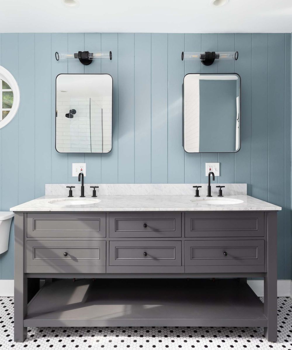 A blue wood panel bathroom with a grey cabinet, white marble countertop, and a black and white hexagon tile floor.