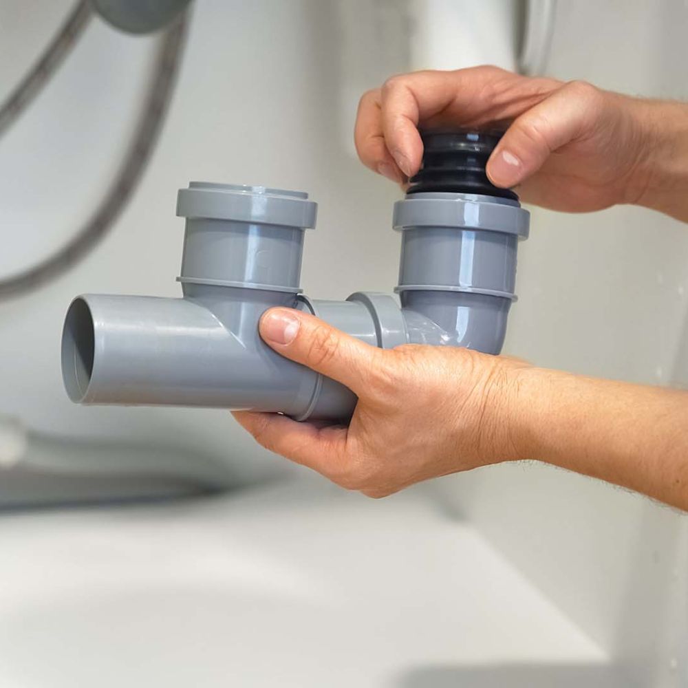 Close up of hands of plumber repairs plumbing pipes sewerage in kitchen sink. Plumbing replacement gasket. Replacement of plumbing pipes.